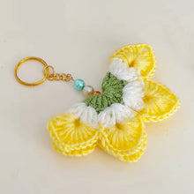 A handmade crochet flower keychain. The flower is composed of various pastel colors, including pink, blue, and green, giving it a vibrant appearance. The petals are textured, showcasing a crochet design that enhances its visual appeal.