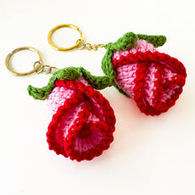 Two crochet rose keychains with pink and red petals and green leaves, handmade with yarn, attached to gold key rings. The roses have intricate detailing and a realistic flower shape, ideal as decorative accessories or gifts.