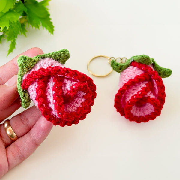Two crochet rose keychains with pink and red petals and green leaves, handmade with yarn, attached to gold key rings. The roses have intricate detailing and a realistic flower shape, ideal as decorative accessories or gifts.