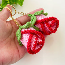 Two crochet rose keychains with pink and red petals and green leaves, handmade with yarn, attached to gold key rings. The roses have intricate detailing and a realistic flower shape, ideal as decorative accessories or gifts.