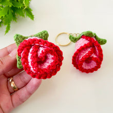 Two crochet rose keychains with pink and red petals and green leaves, handmade with yarn, attached to gold key rings. The roses have intricate detailing and a realistic flower shape, ideal as decorative accessories or gifts.