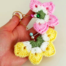 A handmade crochet flower keychain. The flower is composed of various pastel colors, including pink, blue, and green, giving it a vibrant appearance. The petals are textured, showcasing a crochet design that enhances its visual appeal.