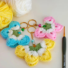 A handmade crochet flower keychain. The flower is composed of various pastel colors, including pink, blue, and green, giving it a vibrant appearance. The petals are textured, showcasing a crochet design that enhances its visual appeal.
