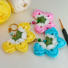 A handmade crochet flower keychain. The flower is composed of various pastel colors, including pink, blue, and green, giving it a vibrant appearance. The petals are textured, showcasing a crochet design that enhances its visual appeal.