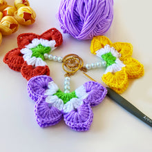 A handmade crochet flower keychain. The flower is composed of various pastel colors, including pink, blue, and green, giving it a vibrant appearance. The petals are textured, showcasing a crochet design that enhances its visual appeal.