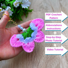 A handmade crochet flower keychain. The flower is composed of various pastel colors, including pink, blue, and green, giving it a vibrant appearance. The petals are textured, showcasing a crochet design that enhances its visual appeal.