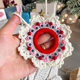 Handmade crochet Christmas wreath ornament with googly eyes and red beads, featuring a playful and festive design, perfect for holiday decor.