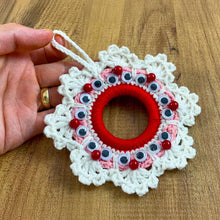 Handmade crochet Christmas wreath ornament with googly eyes and red beads, featuring a playful and festive design, perfect for holiday decor.
