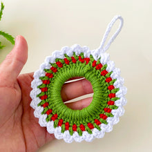 Handmade crochet Christmas wreath ornament with red, green, and white yarn, featuring a beaded loop for hanging. Perfect for holiday home decor or gift wrapping.