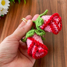 Two crochet rose keychains with pink and red petals and green leaves, handmade with yarn, attached to gold key rings. The roses have intricate detailing and a realistic flower shape, ideal as decorative accessories or gifts.