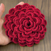 A hand holding a green crochet rose coaster, with white daisies in the background."