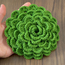 A hand holding a green crochet rose coaster, with white daisies in the background."
