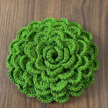 A hand holding a green crochet rose coaster, with white daisies in the background."
