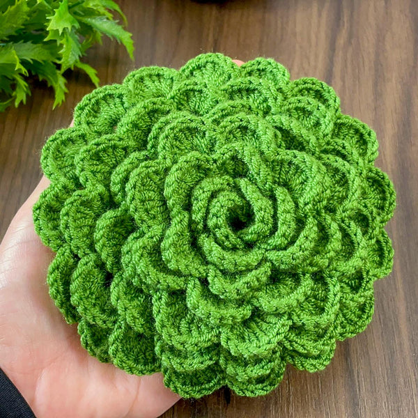 A hand holding a green crochet rose coaster, with white daisies in the background.&quot;